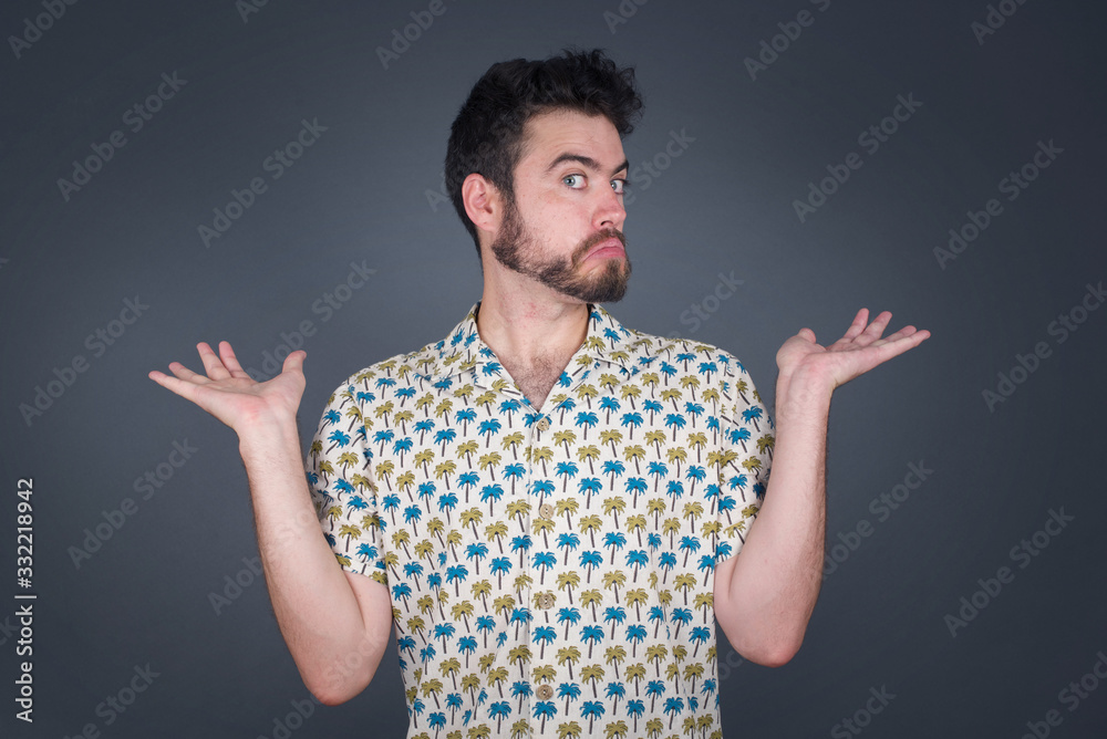 Maybe yes or no. Doubtful fashionable man shrugs shoulders in bewilderment, tries to make decision puzzled what he wants isolated over white concrete wall. Hesitation and uncertainty.