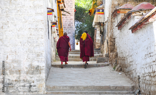 Two Buddhist monks, facing the photographer, go up stairs in a temple in Lhasa, Tibet. The tops of the walls are provided with colored trims.