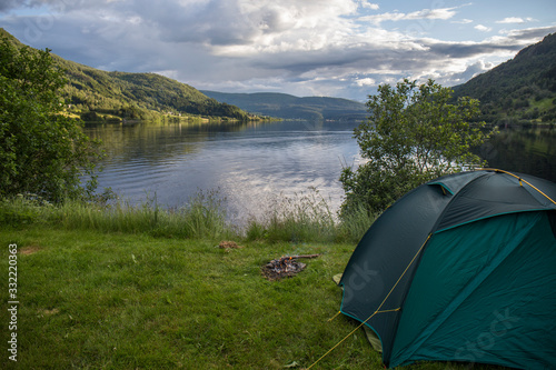 free camping in spectacular scenery, green tent, camping equipment, abundant green vegetation, nordic fjord, blue water, summer days in Norway