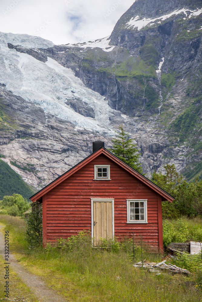 Abandoned village with different colored wooden houses in an idyllic location, between mountains, glacier in the background, abundant green vegetation on a summer day in Norway