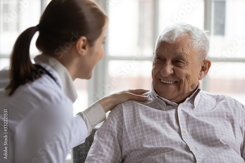 Caring geriatric nurse in white coat cares for grey-haired elderly man in nursing home, listen him relieve solitude, provide support help during visit at home. Homecare eldercare caregiving concept photo