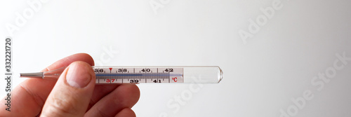 symptoms of coronavirus: a person holds a mercury thermometer in his hand, showing an increase in temperature. light background