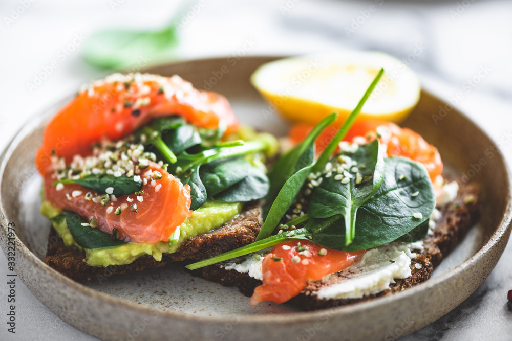 Rye bread toast with avocado, salmon, cream cheese, spinach leaf and hemp seeds on plate. Healthy food. Appetizer, breakfast or snack Rye bread toast with avocado, salmon, cream cheese, spinach leaf and hemp seeds on plate. Healthy food. Appetizer, breakfast or snack