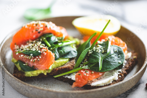 Rye bread toast with avocado, salmon, cream cheese, spinach leaf and hemp seeds on plate. Healthy food. Appetizer, breakfast or snack
