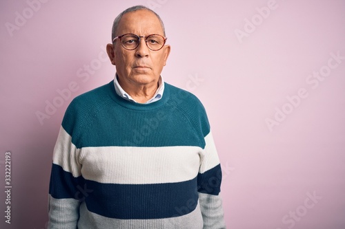 Senior handsome man wearing casual sweater and glasses over isolated pink background with serious expression on face. Simple and natural looking at the camera.