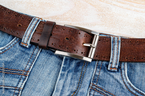 Jeans with brown genuine leather belt with classic metal buckle on a wooden background. Men's stylish leather accessories.