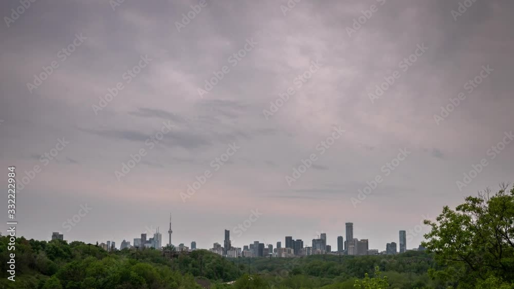 Vertically panning down timelapse of the city skyline in Toronto Canada during sunset with a cloudy pink and blue sky as traffic passes by on a nearby highway surrounded by a forest of trees. Vertically panning down timelapse of the city skyline in Toronto Canada during sunset with a cloudy pink and blue sky as traffic passes by on a nearby highway surrounded by a forest of trees.