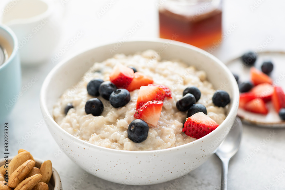 Oatmeal porridge with strawberries and blueberries in white ceramic bowl closeup view. Healthy breakfast food. Vegetarian oatmeal porridge with fresh summer berries Oatmeal porridge with strawberries and blueberries in white ceramic bowl closeup view. Healthy breakfast food. Vegetarian oatmeal porridge with fresh summer berries