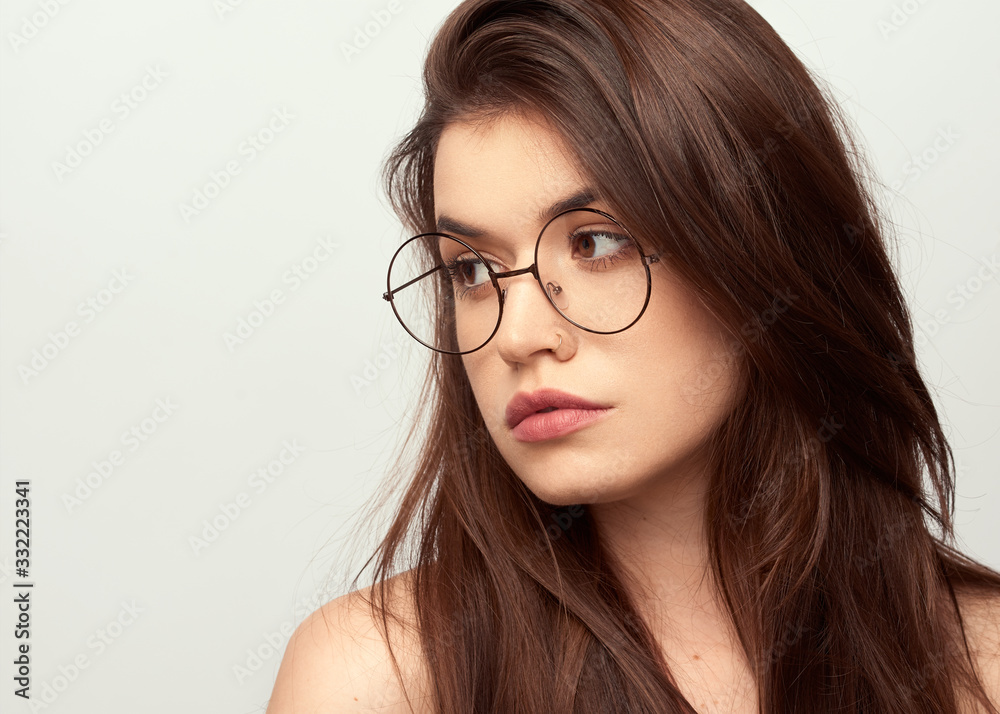 beautiful young girl with brown hair in fashionable glasses posing on a white background with bare shoulders, empty space for text beautiful young girl with brown hair in fashionable glasses posing on a white background with bare shoulders, empty space for text
