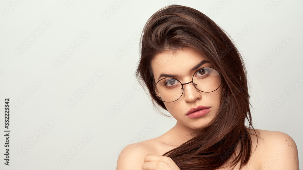 beautiful young girl with brown hair in fashionable glasses posing on a white background with bare shoulders, empty space for text beautiful young girl with brown hair in fashionable glasses posing on a white background with bare shoulders, empty space for text