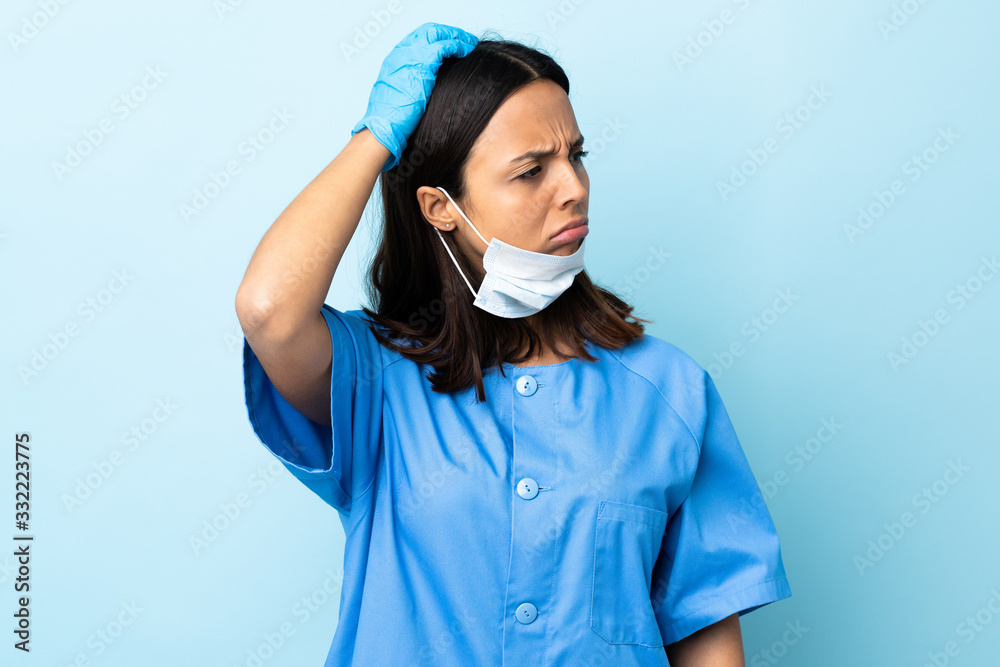 Surgeon woman over isolated blue background having doubts while scratching head Surgeon woman over isolated blue background having doubts while scratching head