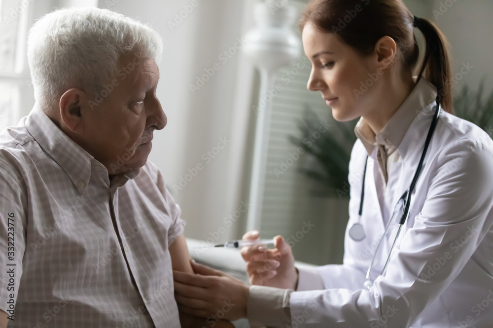Obraz premium Female nurse in white coat use syringe makes injection to old patient. Elderly man receives professional aid. Vaccinations for older people, endorsing immune system, senile diseases eldercare concept