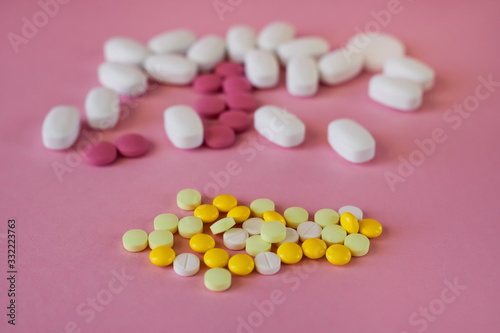 Assorted pharmaceutical medicine pills. Multi-colored pills of different shapes on a light pink background  foreground of white and yellow pills  selective focus.