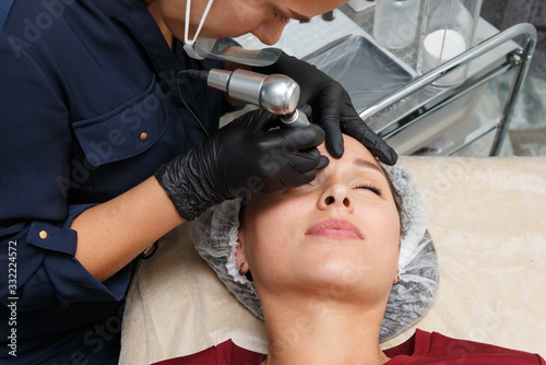 The master applies eyebrow makeup paint to the client with a tattoo machine