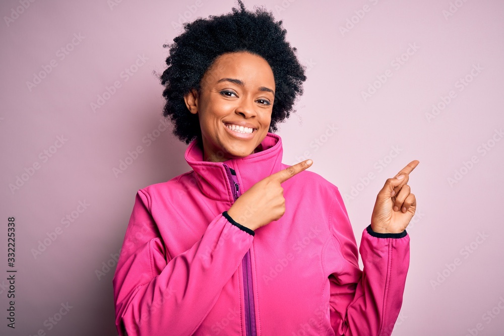 Young African American afro sportswoman with curly hair wearing sportswear doin sport smiling and looking at the camera pointing with two hands and fingers to the side. Young African American afro sportswoman with curly hair wearing sportswear doin sport smiling and looking at the camera pointing with two hands and fingers to the side.