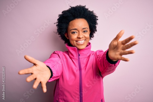 Young African American afro sportswoman with curly hair wearing sportswear doin sport looking at the camera smiling with open arms for hug. Cheerful expression embracing happiness. photo