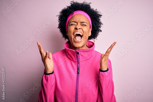 Young beautiful African American afro sportswoman with curly hair wearing pink sportswear celebrating mad and crazy for success with arms raised and closed eyes screaming excited. Winner concept