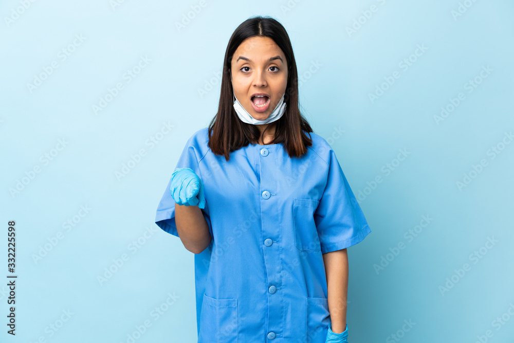 Surgeon woman over isolated blue background surprised and pointing front Surgeon woman over isolated blue background surprised and pointing front
