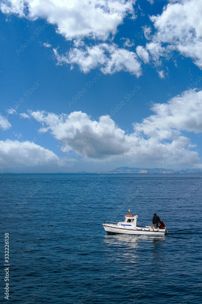 small lonely boat sailing the blue sea, mountains in the background and wonderful clouds