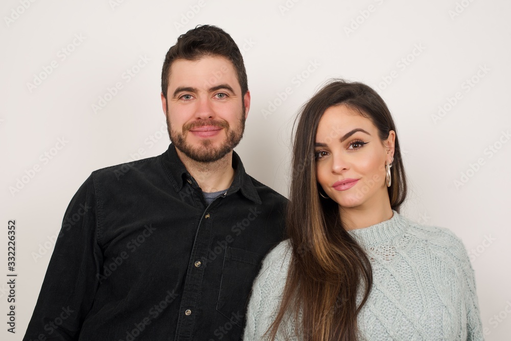 Close up studio shot of beautiful young couple looking at camera with charming cute smile while posing against white blank copy space wall for your content Close up studio shot of beautiful young couple looking at camera with charming cute smile while posing against white blank copy space wall for your content