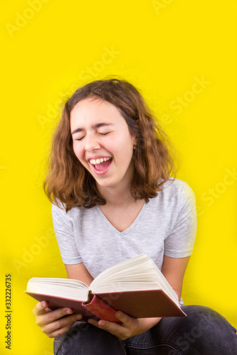 Curly beautiful girl reads a funny book and laughs. Home education
