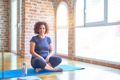 Middle age beautiful sportswoman wearing sportswear sitting on mat practicing yoga at home skeptic and nervous, frowning upset because of problem. Negative person.