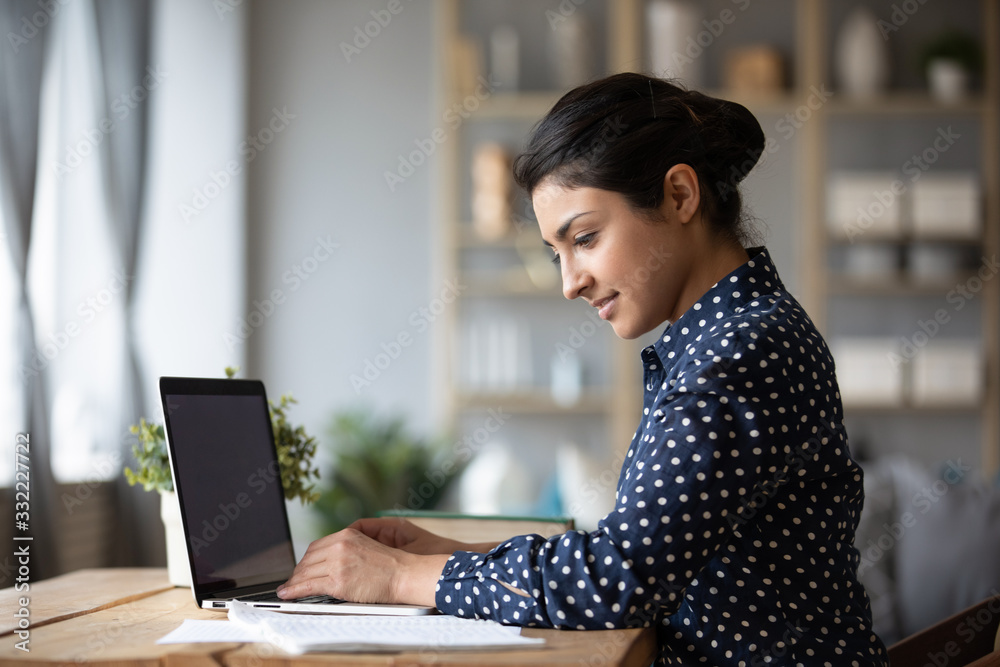 Smiling Indian young woman working on laptop, reading documents ...