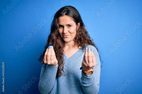 Young beautiful woman with curly hair wearing blue casual sweater over isolated background doing money gesture with hands  asking for salary payment  millionaire business