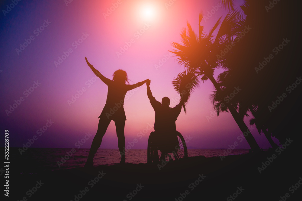 Disabled man in a wheelchair with his wife on the beach. Silhouettes at sunset Disabled man in a wheelchair with his wife on the beach. Silhouettes at sunset
