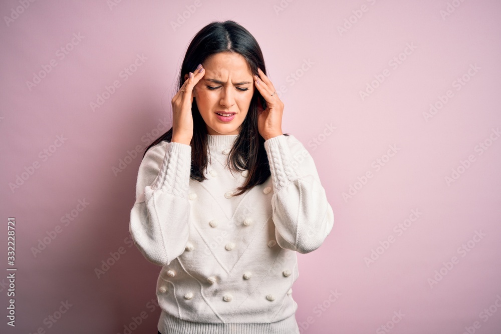 Young brunette woman with blue eyes wearing casual sweater over isolated pink background with hand on head for pain in head because stress. Suffering migraine. Young brunette woman with blue eyes wearing casual sweater over isolated pink background with hand on head for pain in head because stress. Suffering migraine.