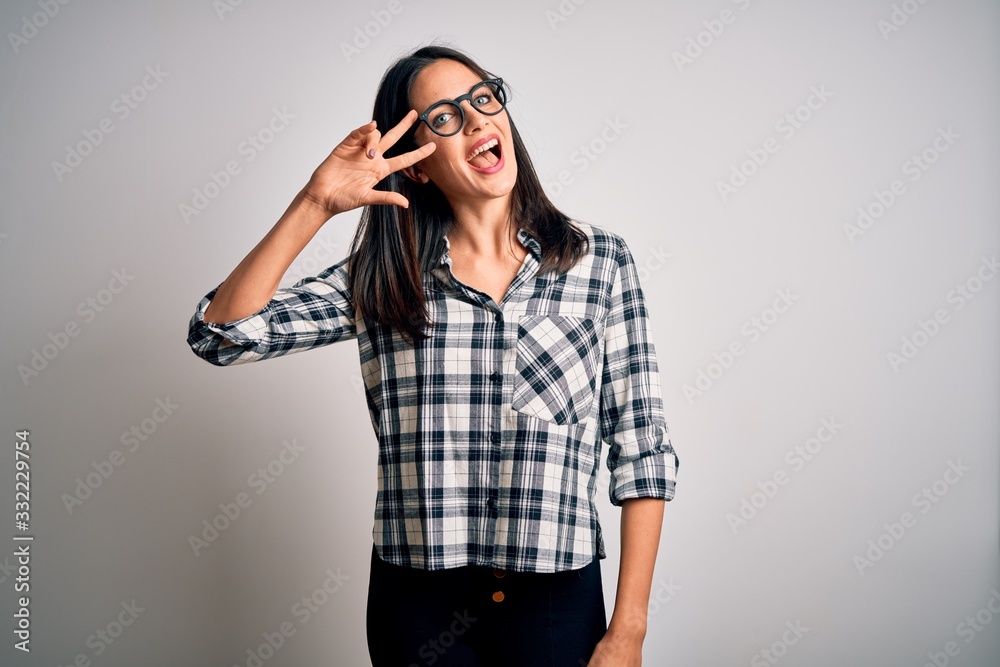 Young brunette woman with blue eyes wearing casual shirt and glasses over white background Doing peace symbol with fingers over face, smiling cheerful showing victory Young brunette woman with blue eyes wearing casual shirt and glasses over white background Doing peace symbol with fingers over face, smiling cheerful showing victory