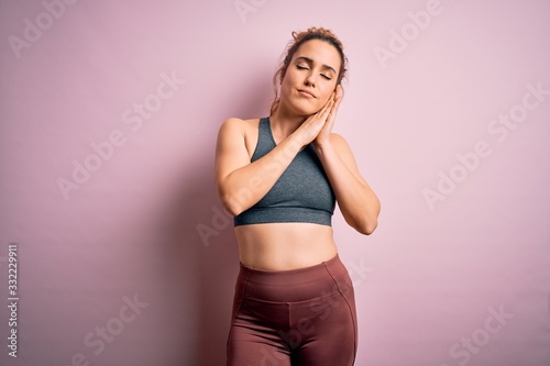 Young beautiful blonde sportswoman doing sport wearing sportswear over pink background sleeping tired dreaming and posing with hands together while smiling with closed eyes.