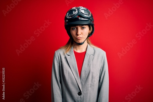 Young beautiful blonde motorcyclist woman wearing motorcycle helmet over red background depressed and worry for distress, crying angry and afraid. Sad expression. © Krakenimages.com