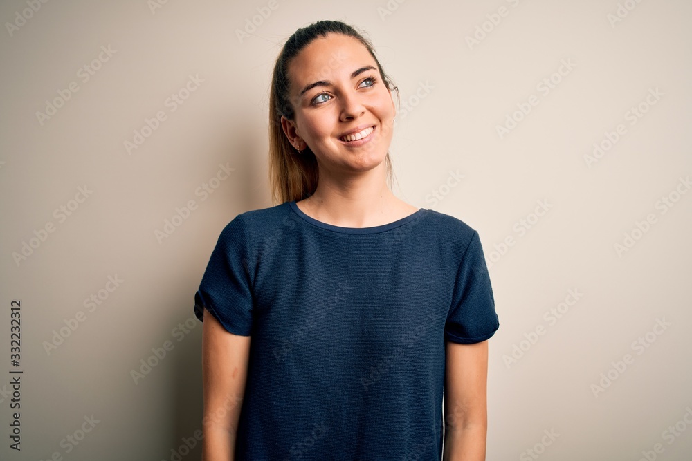 Φωτογραφία Young beautiful blonde woman with blue eyes wearing casual t-shirt over white background looking away to side with smile on face, natural expression