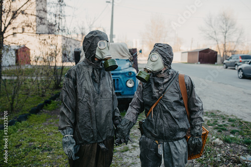 Couple in love holds hands in NBC protective suits and gas masks.