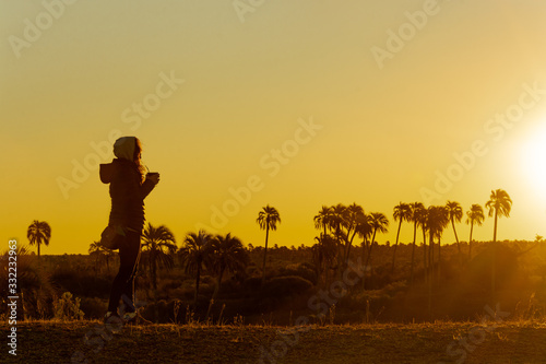 Argentinian woman holding  mate   typical southamerican beverage  in beautiful scenery with palm trees during sunset in El Palmar National Park  Argentina.