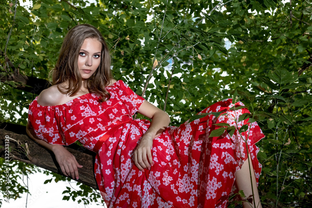 A beautiful young girl with perfect skin, with long hair in a red dress lies on a tree branch with a relaxed A beautiful young girl with perfect skin, with long hair in a red dress lies on a tree branch with a relaxed