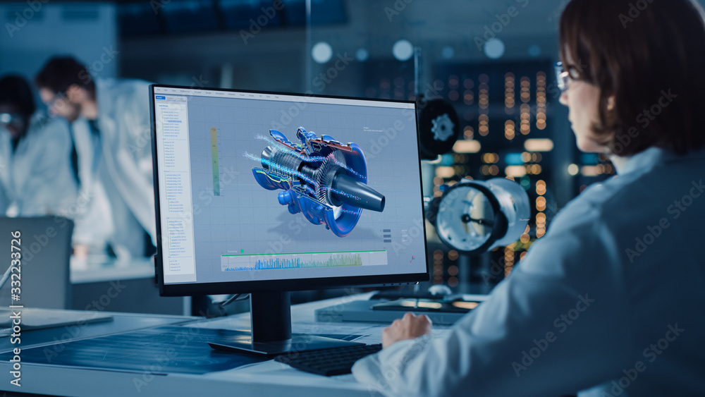 Over the Shoulder Shot: Female IT Scientist Uses Computer Showing CAD Software with Airplane Engine. In the Background Technology Development Laboratory with Scientists, Engineers Working