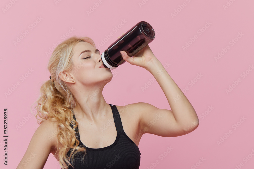 Advertisement personal training. a young sporty woman drinks a protein shake from a shaker after training indoors. Pink background Advertisement personal training. a young sporty woman drinks a protein shake from a shaker after training indoors. Pink background