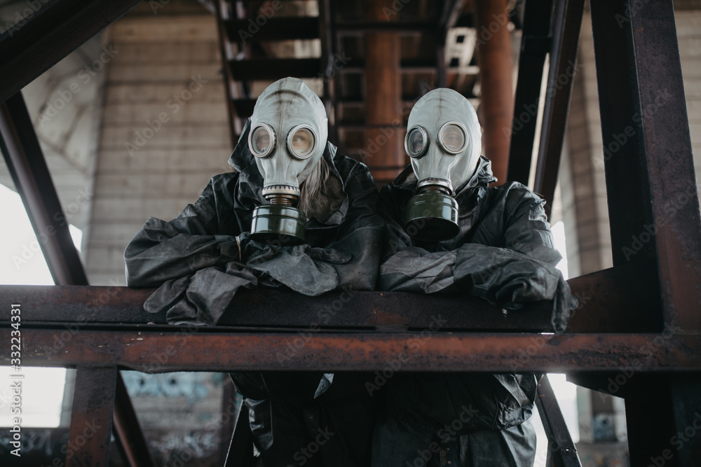 Couple in love stands under bridge in NBC protective suits and gas masks.