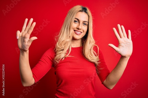 Young beautiful blonde woman wearing casual t-shirt standing over isolated red background showing and pointing up with fingers number nine while smiling confident and happy.