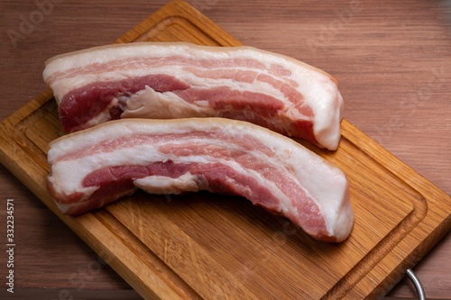 on the cutting Board are two slices of fresh country pork belly. Bacon prepared for salting