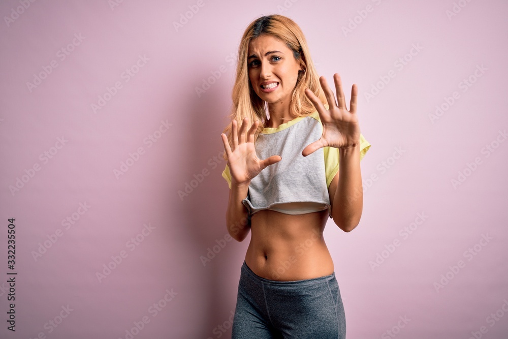 Young beautiful blonde sportswoman doing sport wearing sportswear over pink background disgusted expression, displeased and fearful doing disgust face because aversion reaction. With hands raised Young beautiful blonde sportswoman doing sport wearing sportswear over pink background disgusted expression, displeased and fearful doing disgust face because aversion reaction. With hands raised