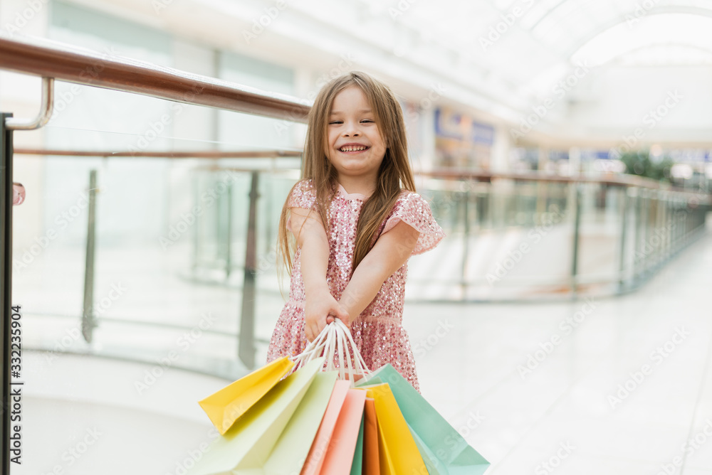 A little girl holds multi-colored pastel bags in her hands. The concept of shopping, shopping in the mall A little girl holds multi-colored pastel bags in her hands. The concept of shopping, shopping in the mall