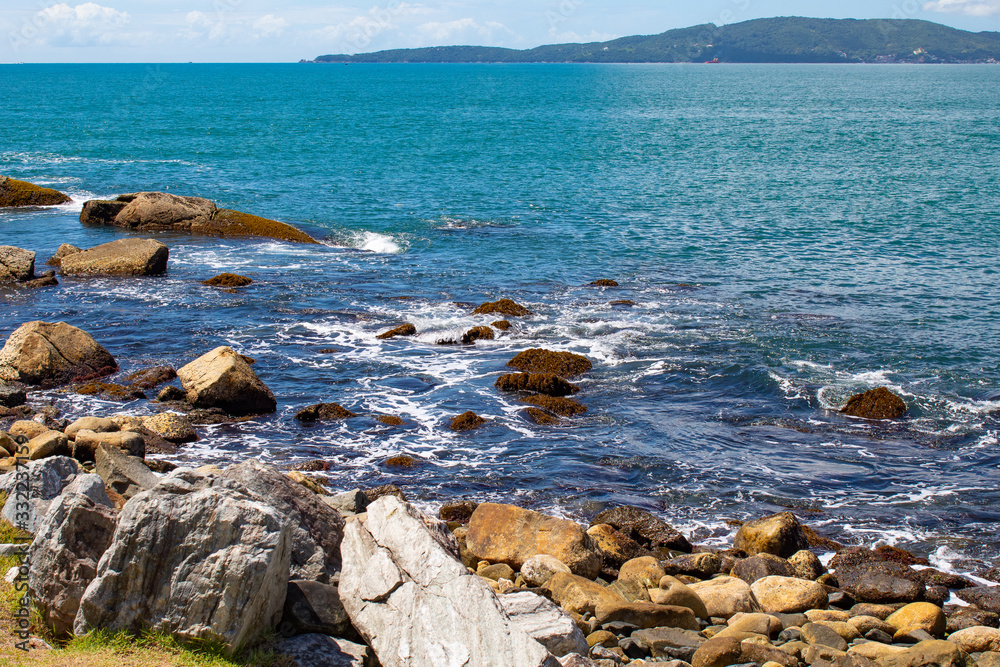 Mar, rochas e céu azul com nuvens na Praia tropical de Ilhota em Itapema, Santa Catarina