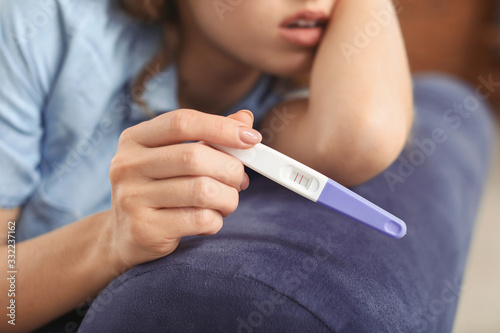 Sad young woman with pregnancy test at home, closeup