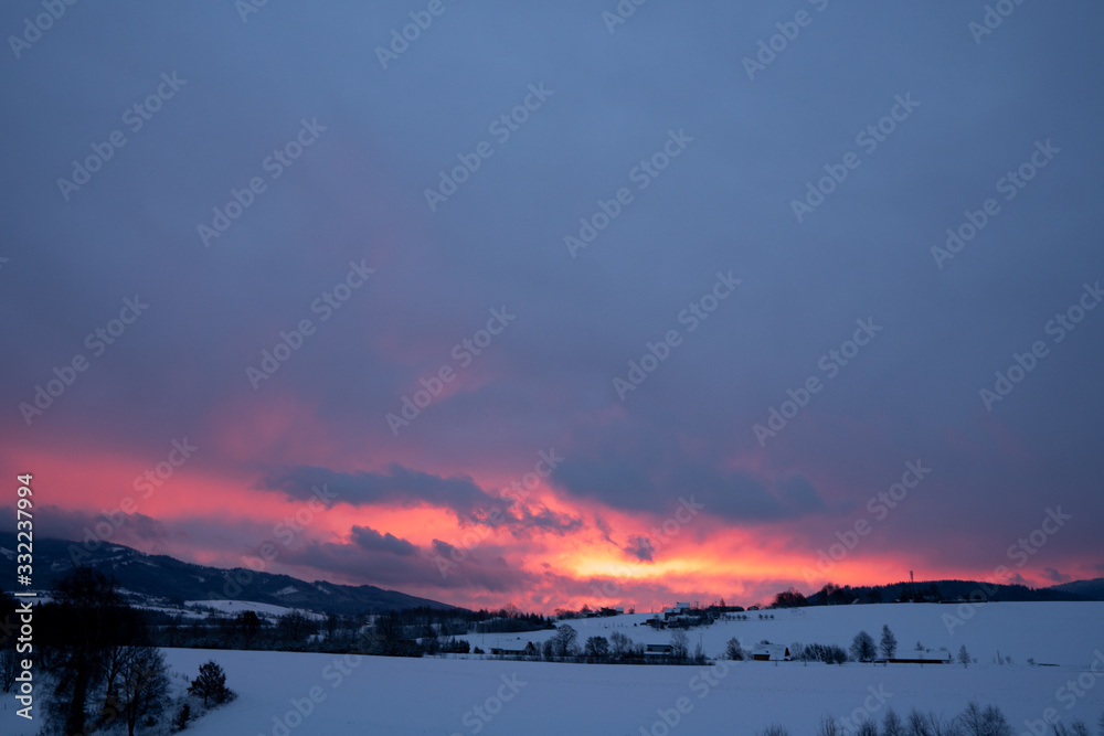 Red clouds at sunrise in winter in the mountains with several houses in the valley