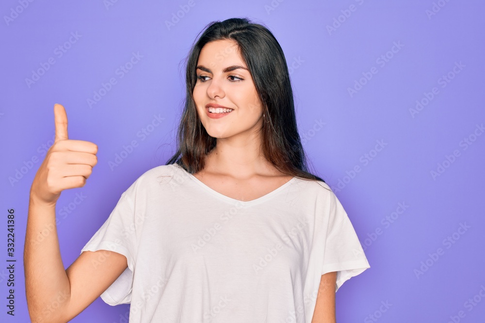 Young beautiful brunette woman wearing casual white t-shirt over purple background Looking proud, smiling doing thumbs up gesture to the side Young beautiful brunette woman wearing casual white t-shirt over purple background Looking proud, smiling doing thumbs up gesture to the side