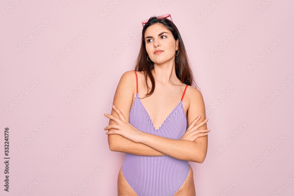 Young beautiful fashion girl wearing swimwear swimsuit and sunglasses over pink background looking to the side with arms crossed convinced and confident Young beautiful fashion girl wearing swimwear swimsuit and sunglasses over pink background looking to the side with arms crossed convinced and confident