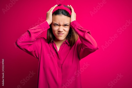 Young beautiful brunette girl wearing casual shirt standing over isolated pink background suffering from headache desperate and stressed because pain and migraine. Hands on head. © Krakenimages.com